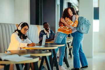 University friends greeting with a warm hug in a modern study area as students engage in academic activities