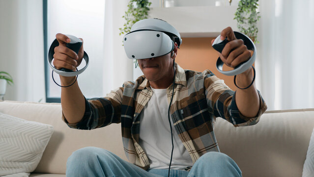 African American man having fun at home couch with virtual reality video game fight guy play 3d cyber gaming fighting with controllers man playing in VR glasses helmet using joysticks metaverse world