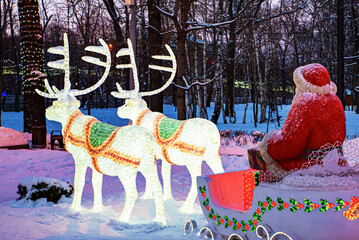Christmas display of illuminated reindeer pulling a sleigh with Santa Claus in a snowy winter park,...