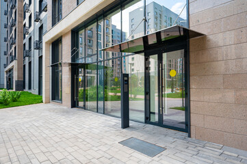 Modern entrance to a residential building with large glass windows, a numeric sign, and paved...
