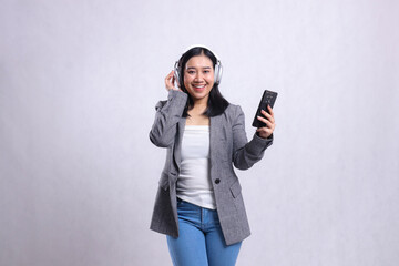 gesture of beautiful adult office woman cheerful wearing headphone while holding and mobile phone wearing suit isolated on white background. concept of advertising, education,entertainment, technology