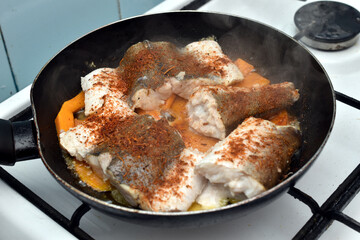 The fish, cut into pieces, is fried in a pan with spices and pieces of pumpkin.