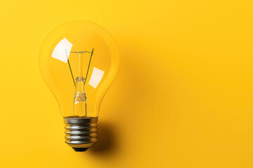 Close-up of a clear incandescent light bulb against a bright yellow background, emphasizing creativity and innovation concepts.