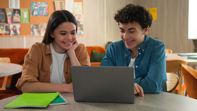 Two students friends Caucasian girl female schoolgirl boy guy male schoolboy together studying learning online laptop internet class lesson prepare exams talking laughing cooperation smiling school