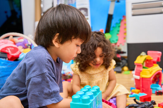 Latino siblings playing with toys and building blocks indoors.