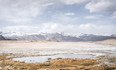 Panoramic landscape of textured Tien Shan mountains in Pamir in Tajikistan, landscape of a mountain range with snow and glaciers in summer, a small lake and reflection of mountains in it