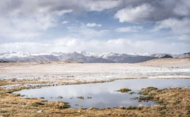 Panoramic landscape of textured Tien Shan mountains in Pamir in Tajikistan, landscape of a mountain range with snow and glaciers in summer, a small lake and reflection of mountains in it