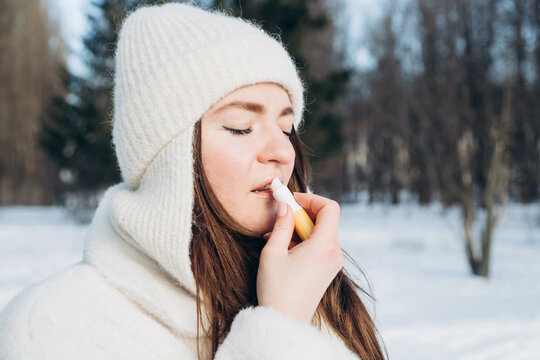 Woman applying lip balm outdoors in winter. Portrait of a beautiful woman with application of the protective cream to the lips.