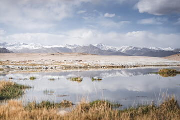 Panoramic landscape of textured Tien Shan mountains in Pamir in Tajikistan, landscape of a mountain range with snow and glaciers in summer, a small lake and reflection of mountains in it