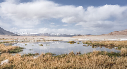 Panoramic landscape of textured Tien Shan mountains in Pamir in Tajikistan, landscape of a mountain range with snow and glaciers in summer, a small lake and reflection of mountains in it