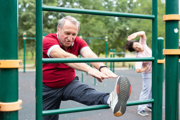 Naklejka premium Elderly man doing leg stretching on the outdoor sports ground