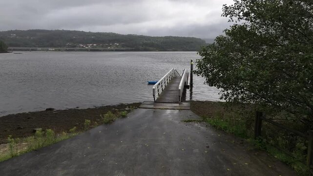 Pantalan con un barco amarrado azul en mitad de una ria