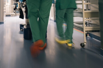 A blurred capture of two doctors or nurses in green scrubs moving quickly down a hospital hallway