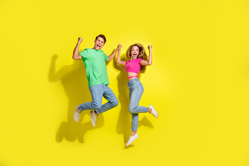 Full size photo of two nice young people hold arms jump raise fists isolated on bright yellow color background