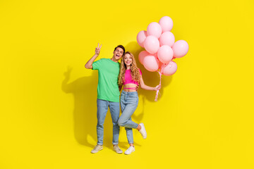 Full size photo of two nice young people show v-sign hold balloons isolated on bright yellow color background