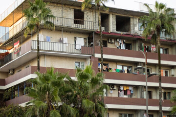 A residential apartment building in Batumi with clothes hanging from balconies, palm trees in the foreground, and an unfinished top floor