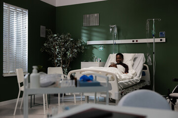 Resting in her hospital bed, the young African woman chuckles as she engages with her phone.
