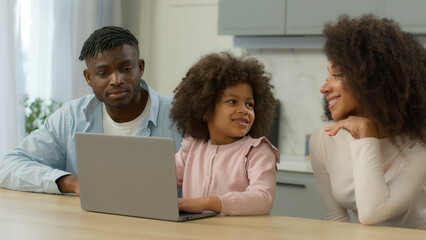 African American family at kitchen shopping online together mother father teach child daughter little girl at home kitchen using laptop food delivery kid computer playing e-learning parental control