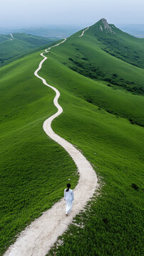 jeune femme marchant de dos le long d'un chemin sinueux entour&eacute; d'herbe