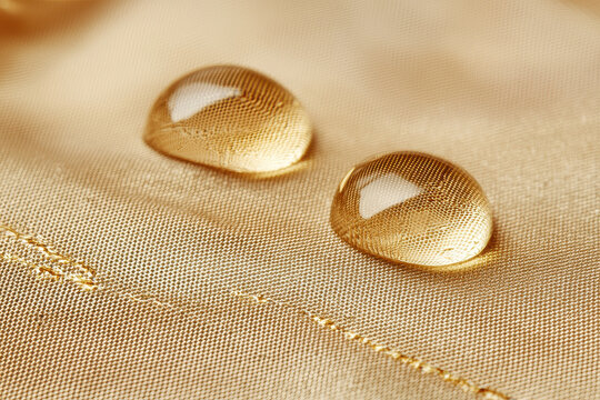 Golden droplets of liquid rest delicately on a textured, smooth fabric, creating a captivating abstract image that accentuates elegance and luxury.