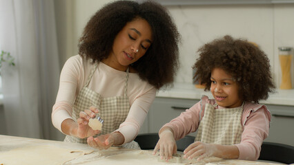 Happy African American family mother mom woman female with little girl daughter child kid cooking together at kitchen cook baking fun holiday teaching make cookie mold cut out forms of dough food