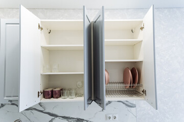 A kitchen cabinet featuring its doors wide open, showcasing a dish drying rack placed inside, indicating a space actively used for preparing meals and cleaning up afterward