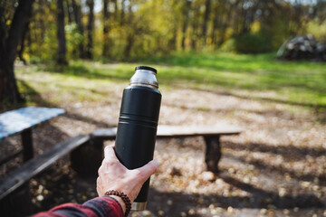 In a picturesque park teeming with vibrant greenery, a person stands proudly holding a thermos...