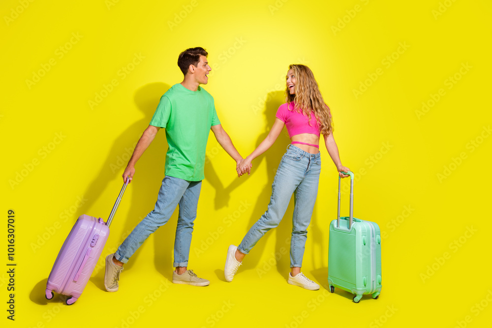 Wall mural full size photo of two nice young people hold arms suitcase isolated on bright yellow color backgrou