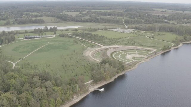 Aerial shot of a sprawling park with paths, open fields, and a lakeside shoreline, captured in 4K log format for high dynamic range.