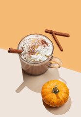 Spice  latte in glass cup on orange background with decorative pumpkin, cinnamon sticks and shadows.