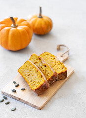 Pumpkin sweet bread or cake with icing on a wooden board on a light background with decorative pumpkins and seeds.