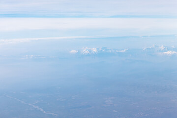 Fototapeta premium Aerial view of snowy mountain tops covered in clouds. Majestic blue mountains view from above 
