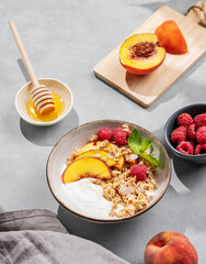 Natural yogurt with oat granola, peach, raspberry and honey in a bowl on a blue background