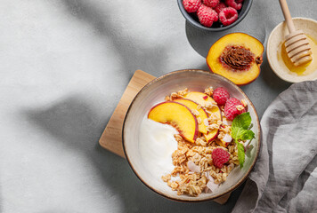 Natural yogurt with oat granola, peach, raspberry and honey in a bowl on a light background