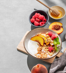 Natural yogurt with granola, peach, raspberry and honey in a bowl on a light background