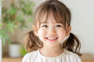 A cheerful girl smiles brightly, showcasing her playful spirit and innocence in a lively indoor setting with green plants.