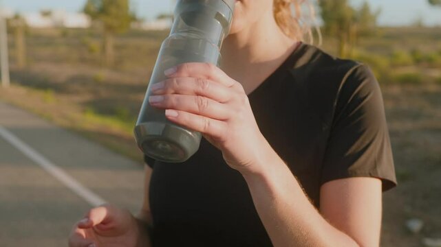 Sport woman is drinking water and cooldown after running in the park