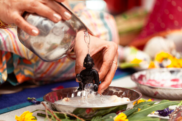 Indian woman performing snan ritual by pouring 'Ganga Jal' on (Laddu Gopal) Hindu god Krishna, during the Indian festival of Krishna Janmashtami.