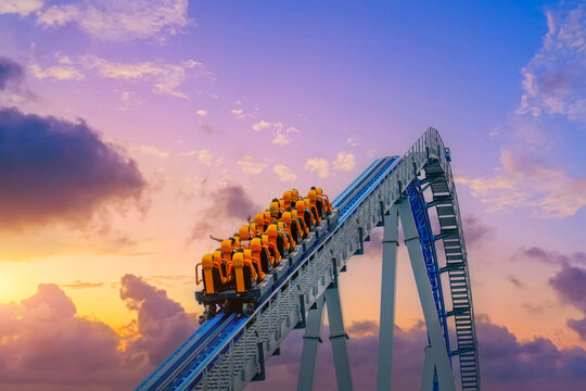 Roller coaster cart with people riding goes through the cart rises high into the air before descending sharply into steep dive against backdrop sunset sky clouds