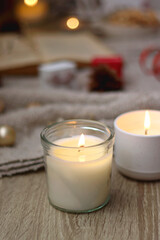 Various Christmas decorations, lit candles, cup of tea or coffee, cookies, books, presents and soft blanket on the table. Holiday hygge at home. Selective focus.