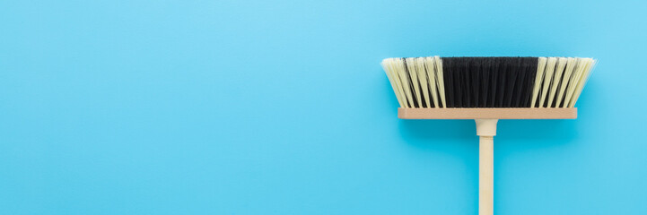 New white black broom with wooden stick on light blue table background. Pastel color. Wide banner....