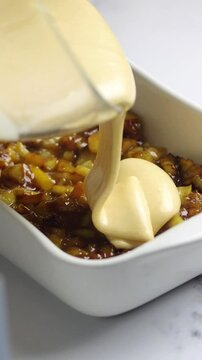 Adding creamy batter over caramelized apples in a baking dish. Perfect for dessert preparation videos, cooking blogs, and recipe tutorials. Cooking apple pie