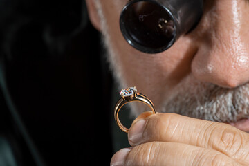 Jewelry appraiser examines a gold ring evaluating large diamond looking through magnifying glass...