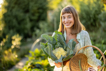 A woman smiles warmly as she holds a freshly harvested cauliflower from her garden. The photo...