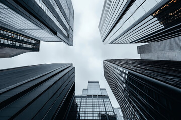 Fototapeta premium Low-angle view of tall modern skyscrapers with reflective glass windows in a cityscape, converging towards a cloudy sky.