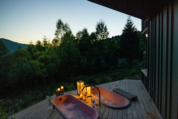 A serene evening setup featuring two pink bubble baths on a wooden deck, surrounded by candlelight....