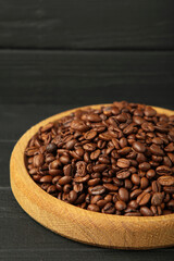 Coffee beans on wooden plate on black wooden background. Vertical photo