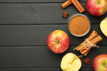 Red apple, cinnamon sticks and cinnamon in bowl on black wooden background.