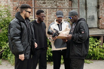 Group of filmmakers collaborating, discussing filming details outside. Diversity in team, with...