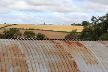 A photograph of the top of a corrugated iron barn with rolling autumn fields of crops in the...
